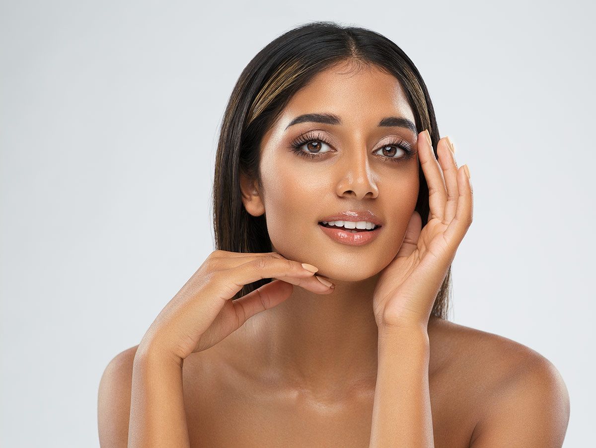 Smiling hydrafacial patient model with hand on face, neutral background.