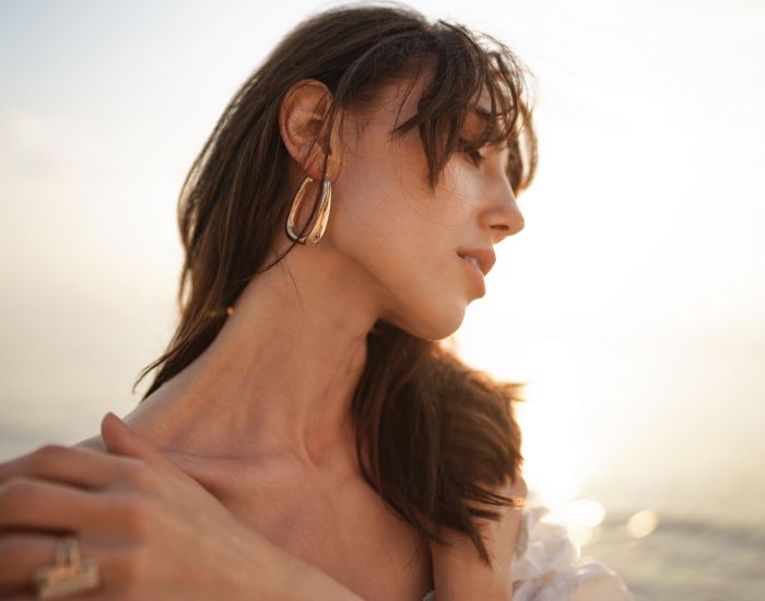 Woman with earrings by the seaside at sunset.
